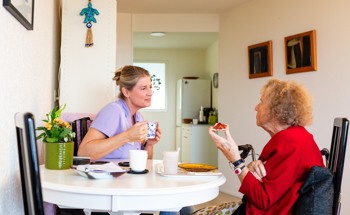 Zorgmedewerker drinkt koffie met oudere dame VPT verpleeghuiszorg thuis